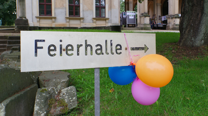 Feierhalle-Schild auf dem Friedhof mit Luftballons dran