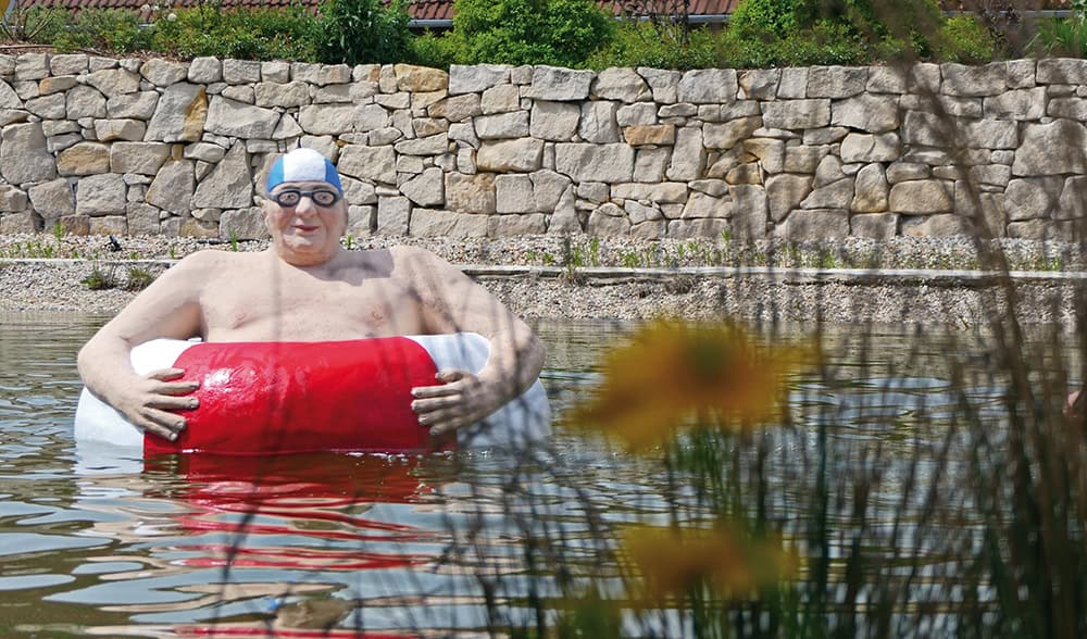 Alltagsmensch älterer Herr mit Badekappe und Schwimmring im Teich