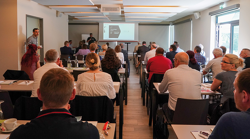 Beim Symposium, alle Teilnehmenden sitzen und blicken nach vorn, fotografiert von hinten