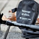 Foto schwarze Klappschaufel mit der Aufschrift „Vorsorge ist alles” als Merchandise, dahinter die Schaufel-Verpackung mit gleicher Aufschrift
