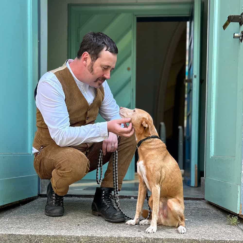 Eric Wrede hockt neben seinem rot-braunen Hund und grault dessen Kinn, beide schauen sich an und lächeln, Foto: privat