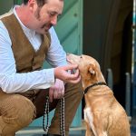 Eric Wrede hockt neben seinem rot-braunen Hund und grault dessen Kinn, beide schauen sich an und lächeln, Foto: privat