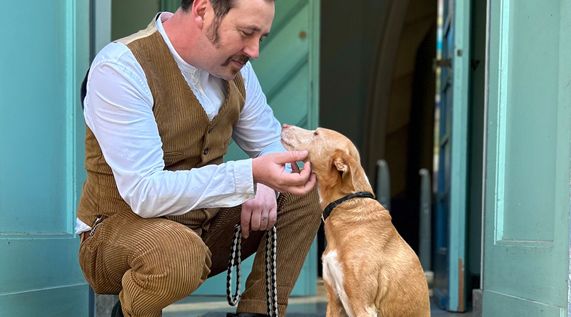 Eric Wrede hockt neben seinem rot-braunen Hund und grault dessen Kinn, beide schauen sich an und lächeln, Foto: privat