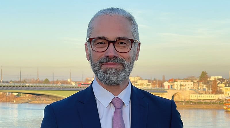 Porträtfoto Prof. Dr. Dr. Tade Spranger im blauen Anzug vor Fluß und Häusern