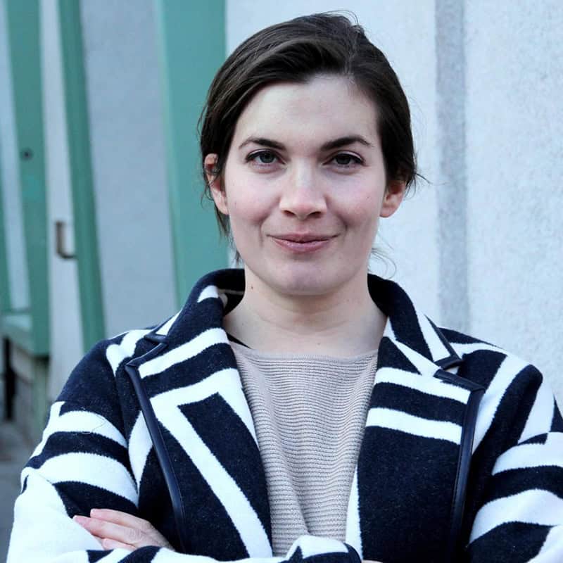 Portraitfoto Valerie Tiefenbacher von Greta Egle, Valerie ist draußen an einer Hauswand, lächelt mit verschränkten Armen in die Kamera