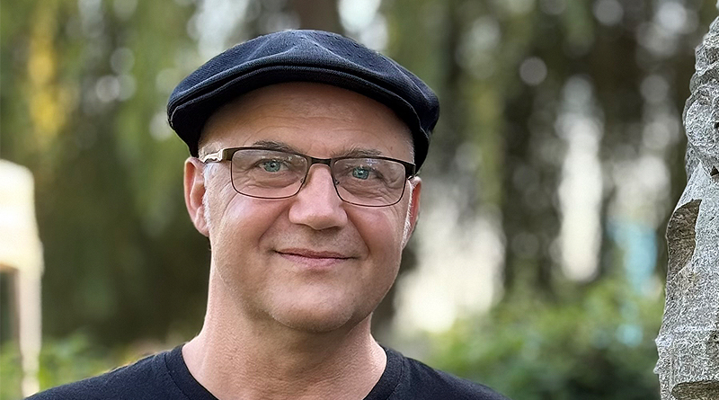 Porträtfoto Dirk Rotzsch von Jörn Rohrberg, Dirk steht neben einer Steinskultur und lächelt in die Kamera, er trägt ein Shirt von The Cure