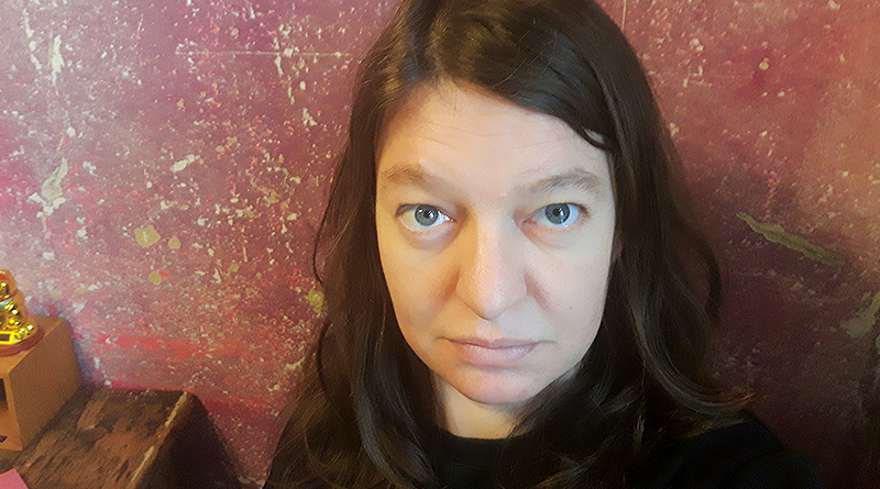 Portraitfoto Juliane Streich, Nahaufnahme, Juliane schaut von unten nach oben in die Kamera, lila-dunkelrosaer Hintergrund, indoor, Foto: privat